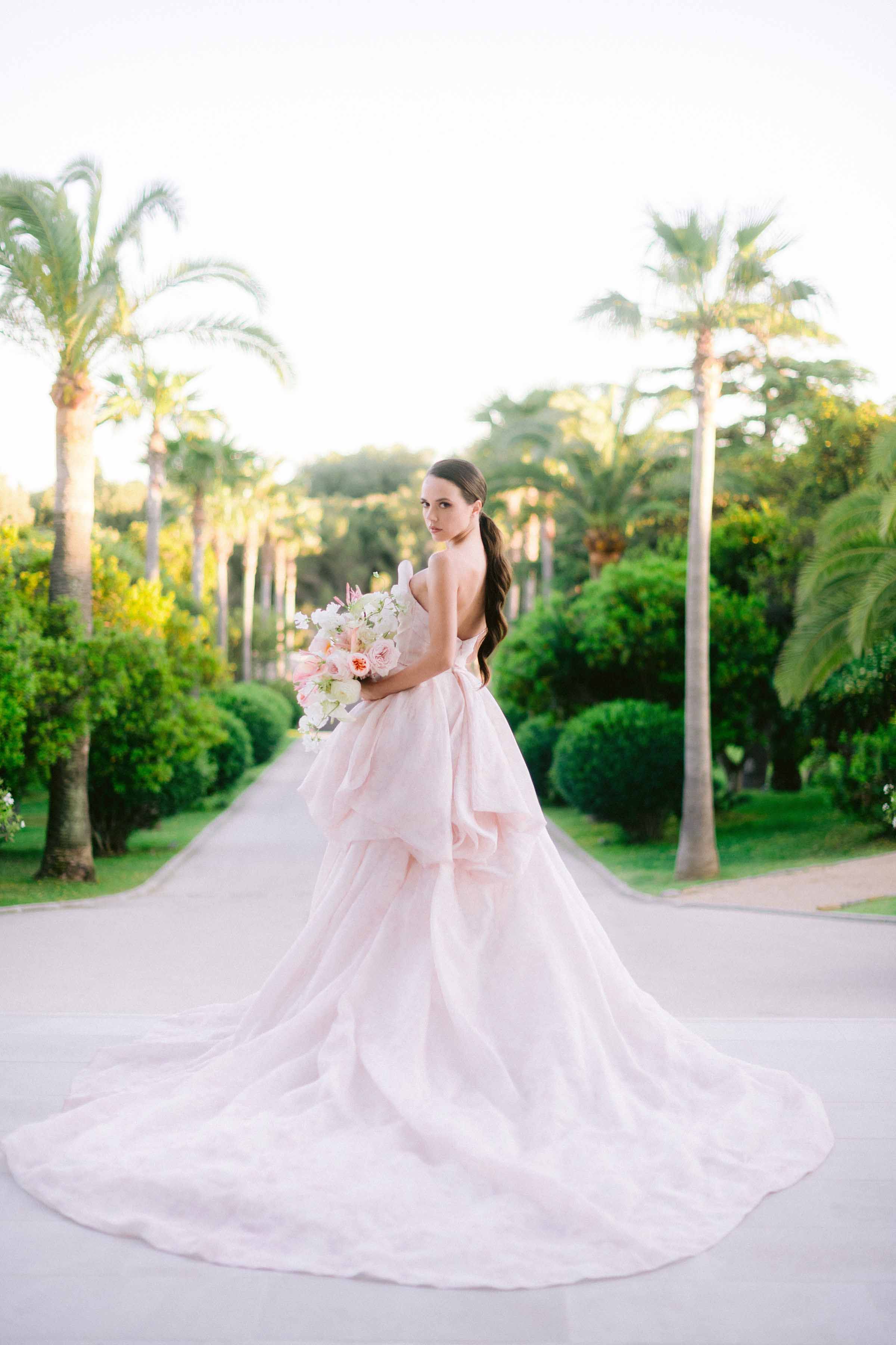 une mariée devant des palmier pose avec sa superbe robe de mariage